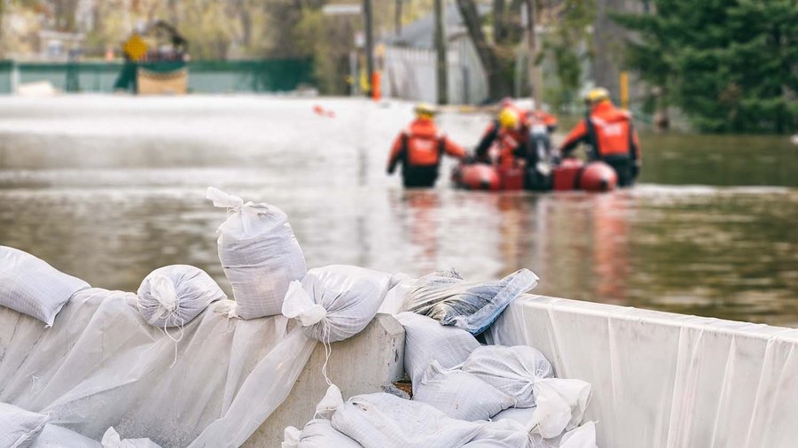 Σάκοι άμμου με πλημμυρισμένα σπίτια και ομάδα διάσωσης στο φόντο 