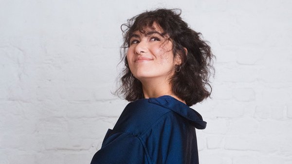 Γυναίκα με μπλε πουκάμισο και καστανά μαλλιά κοιτάει πάνω πονηρά.