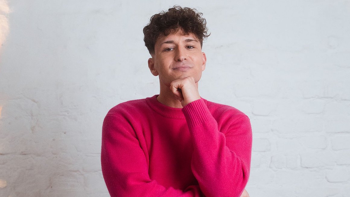 Άνδρας με ροζ πουλόβερ κοιτάζει σκεπτικά την κάμερα