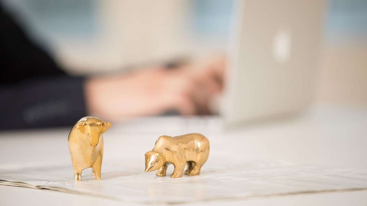 Ένας χρυσός ταύρος και μια χρυσή αρκούδα στέκονται μπροστά από έναν φορητό υπολογιστή σε ένα γραφείο.