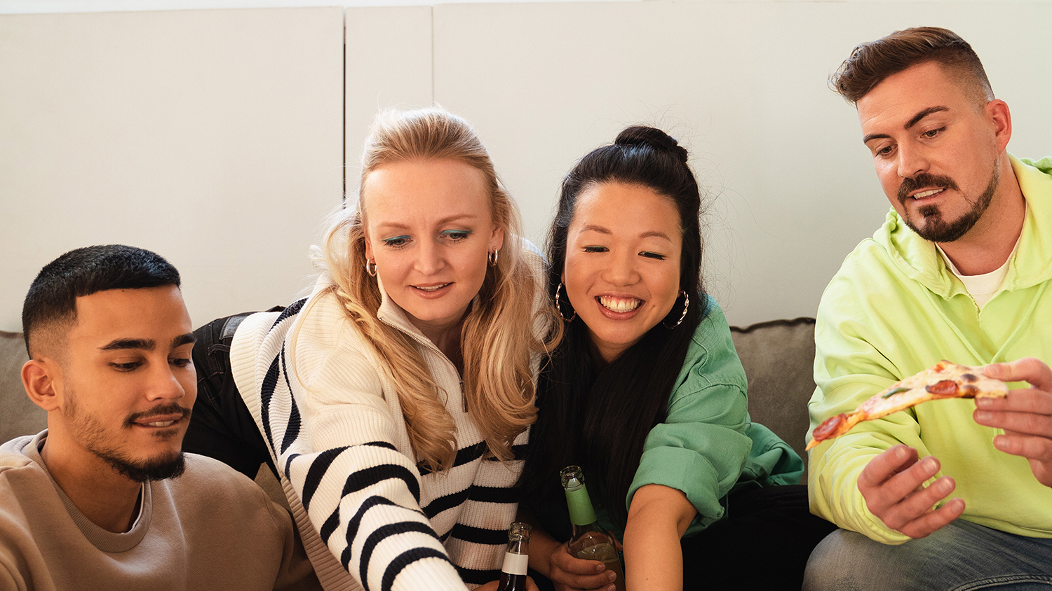 Τέσσερις νέοι κάθονται μαζί σε έναν καναπέ και γελάνε