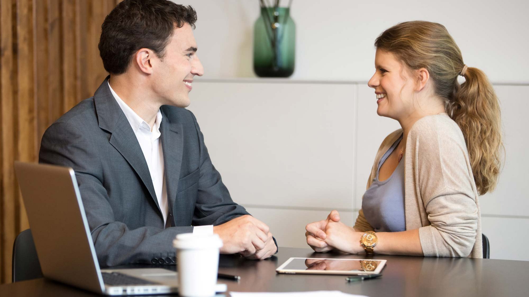 Σύμβουλος συζητά με πελάτισσα σε γραφείο, με φορητό υπολογιστή και έγγραφα στο τραπέζι, σε ήρεμο και συνεργατικό περιβάλλον συμβουλευτικής.