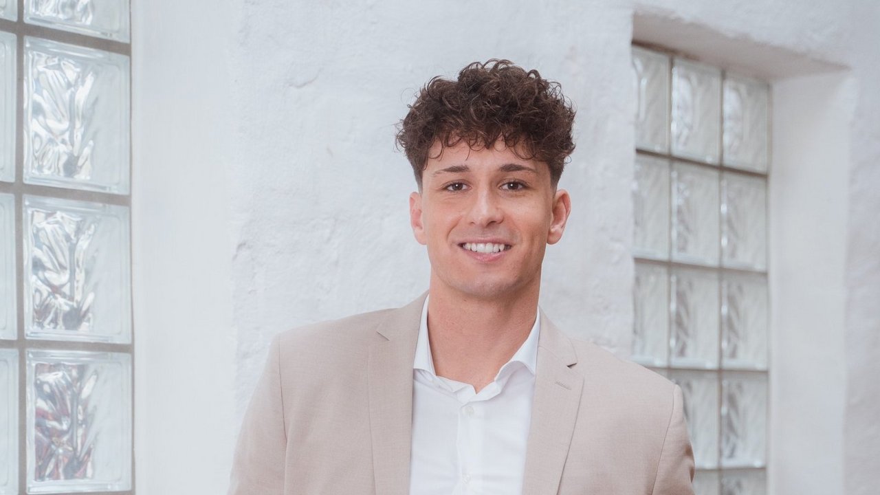 Επαγγελματίας σύμβουλος με κοστούμι σε μπεζ απόχρωση, χαμογελαστός σε ένα σύγχρονο και φωτεινό περιβάλλον γραφείου.