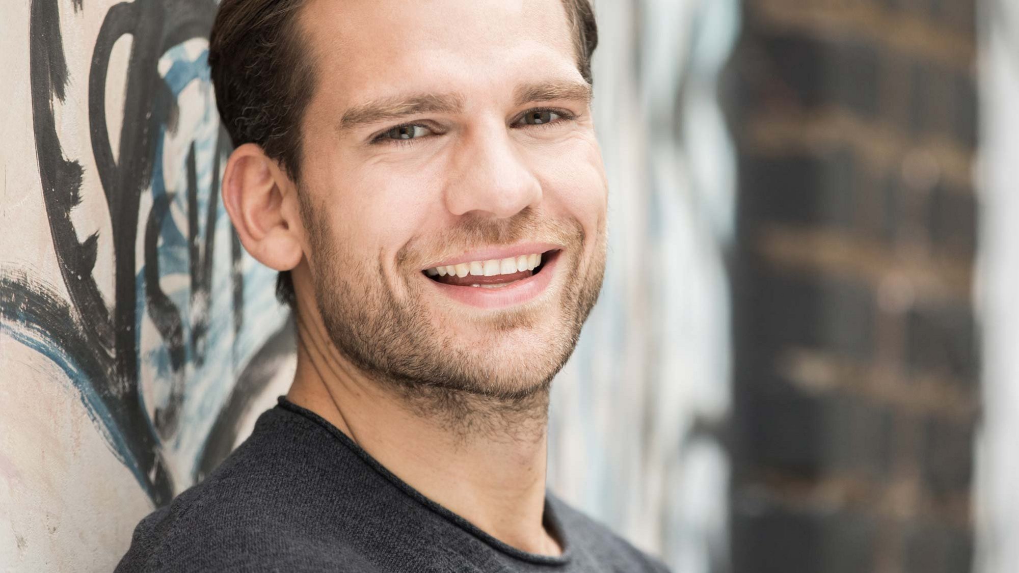 Άτομο που στέκεται μπροστά σε τοίχο με graffiti, σε ύφος κατάλληλο για επαγγελματική παρουσία σε σύγχρονο περιβάλλον.