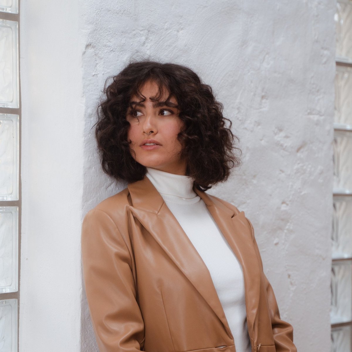 Άτομο σε minimal εξωτερικό φόντο με μοντέρνα εμφάνιση Άτομο με καφέ σακάκι και λευκό ζιβάγκο που στέκεται δίπλα σε ανοιχτόχρωμο τοίχο.